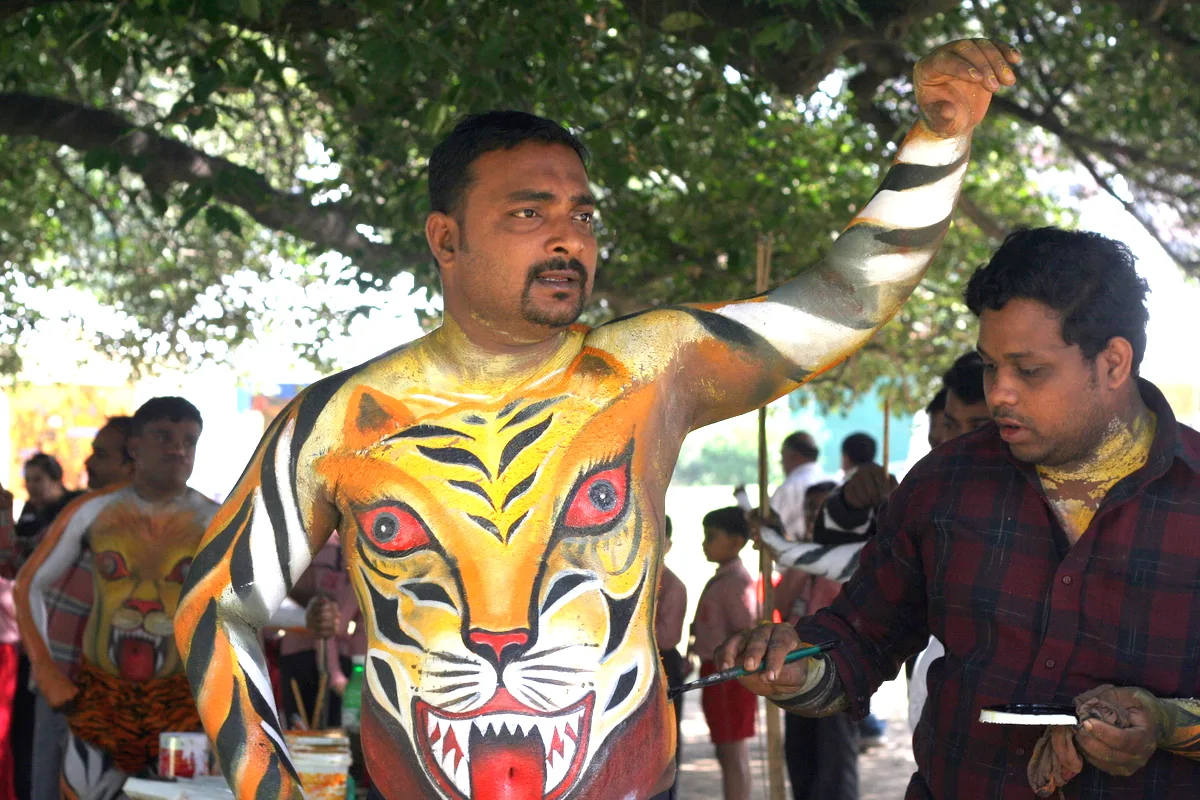 Artist painting tiger stripes on a Pulikali performer’s back.