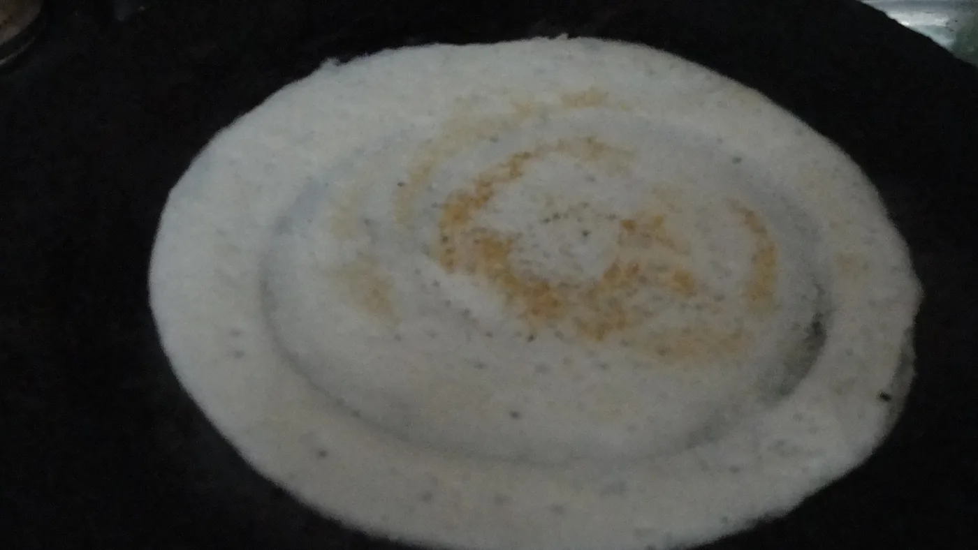 A thin dosa cooking on a hot tava.